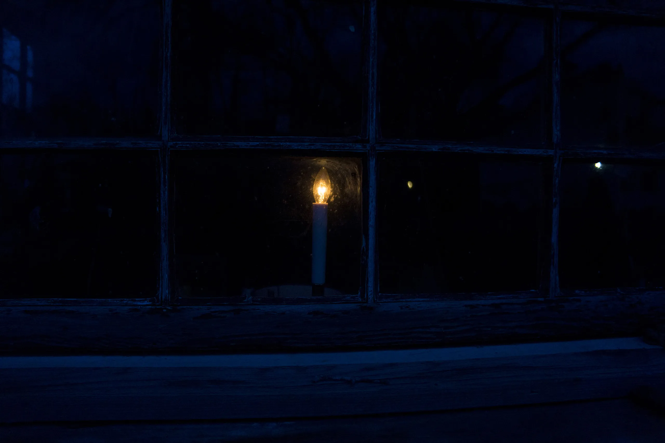 A candle glowing behind a window